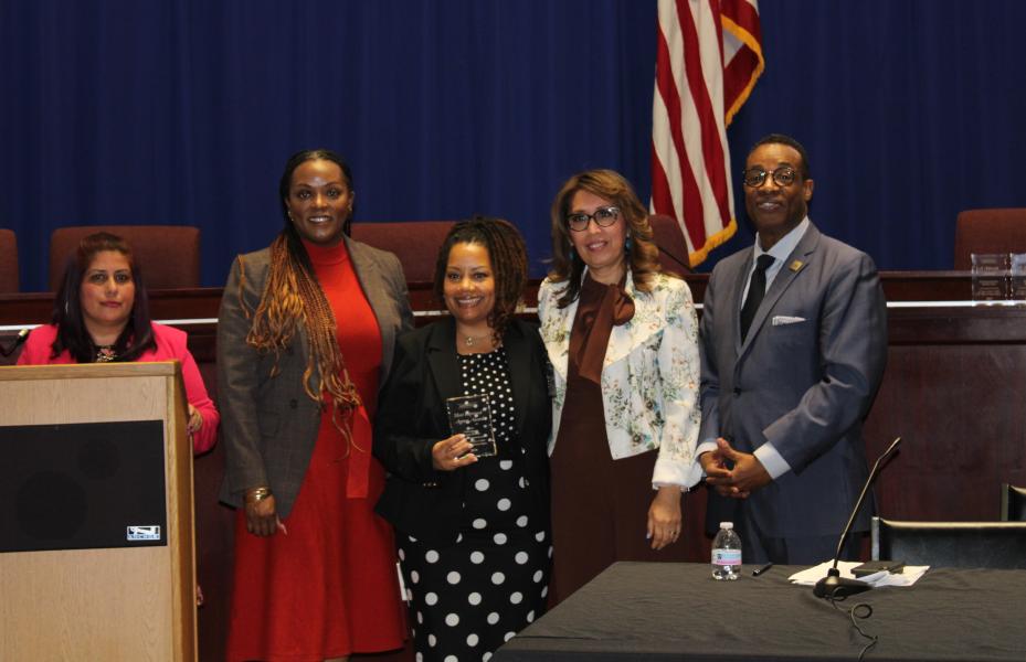 There are five people, two on each side of the middle person who is receiving an award. 
