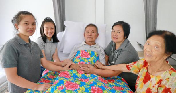 Asian family around hospital bed with older male family member in it 